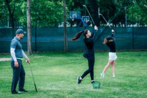 Golf swing technique – golf instructor working with two young ladies on a golf range